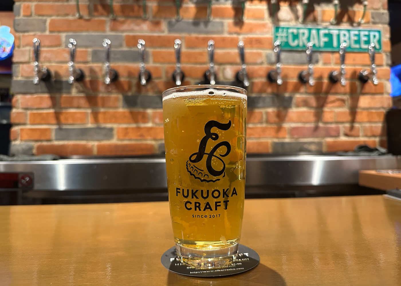 Ett glas med ljus öl på en bardisk. Text på glaset lyder "Fukuoka Craft".