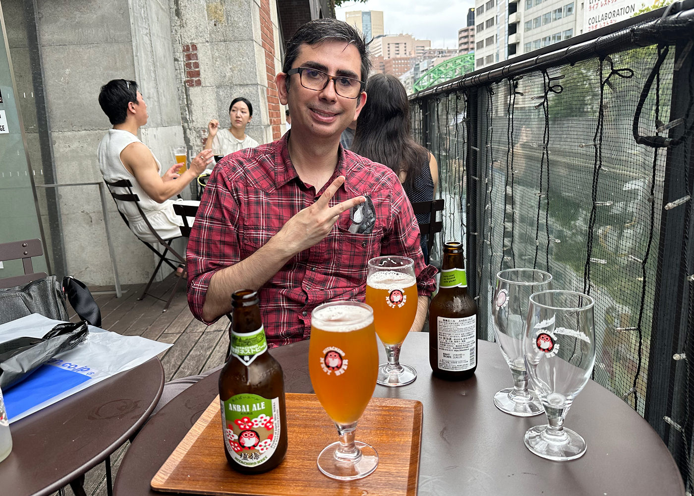 Latinamerikansk man med röd skjorta och glasögon sitter vi ett bird med flera ölglas på. Han ler och visar fredstecknet.