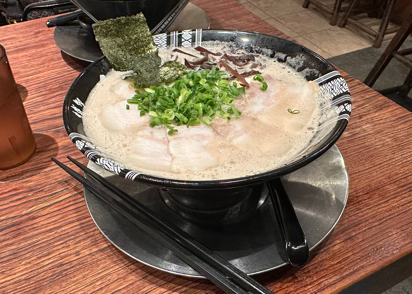 Svart skål med ramen med ljus sås garnerad med fläskkött, sjögräs och gräslök.