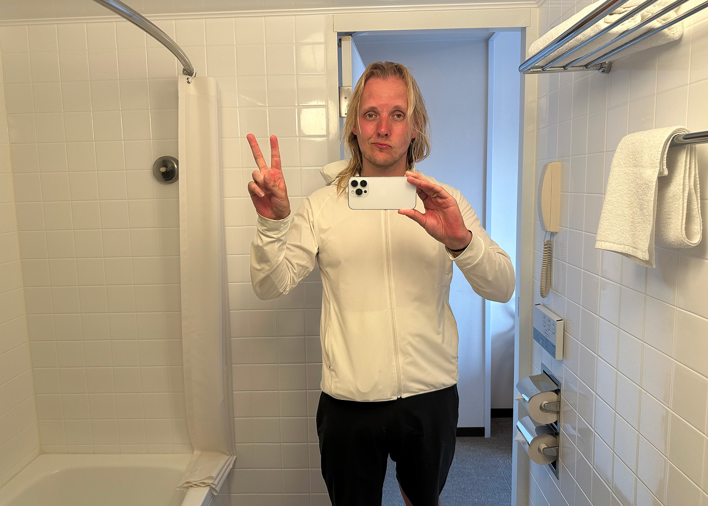 Jag tar en bild på mig själv inuti ett badrum. Jag har svettigt hår och en vit tunn sportjacka på mig.
