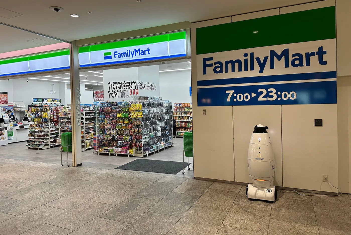 Ett litet snabbköp med stora dörrar och flera hyllor med olika färggranna påsar. En skylt lyder "FamilyMart".