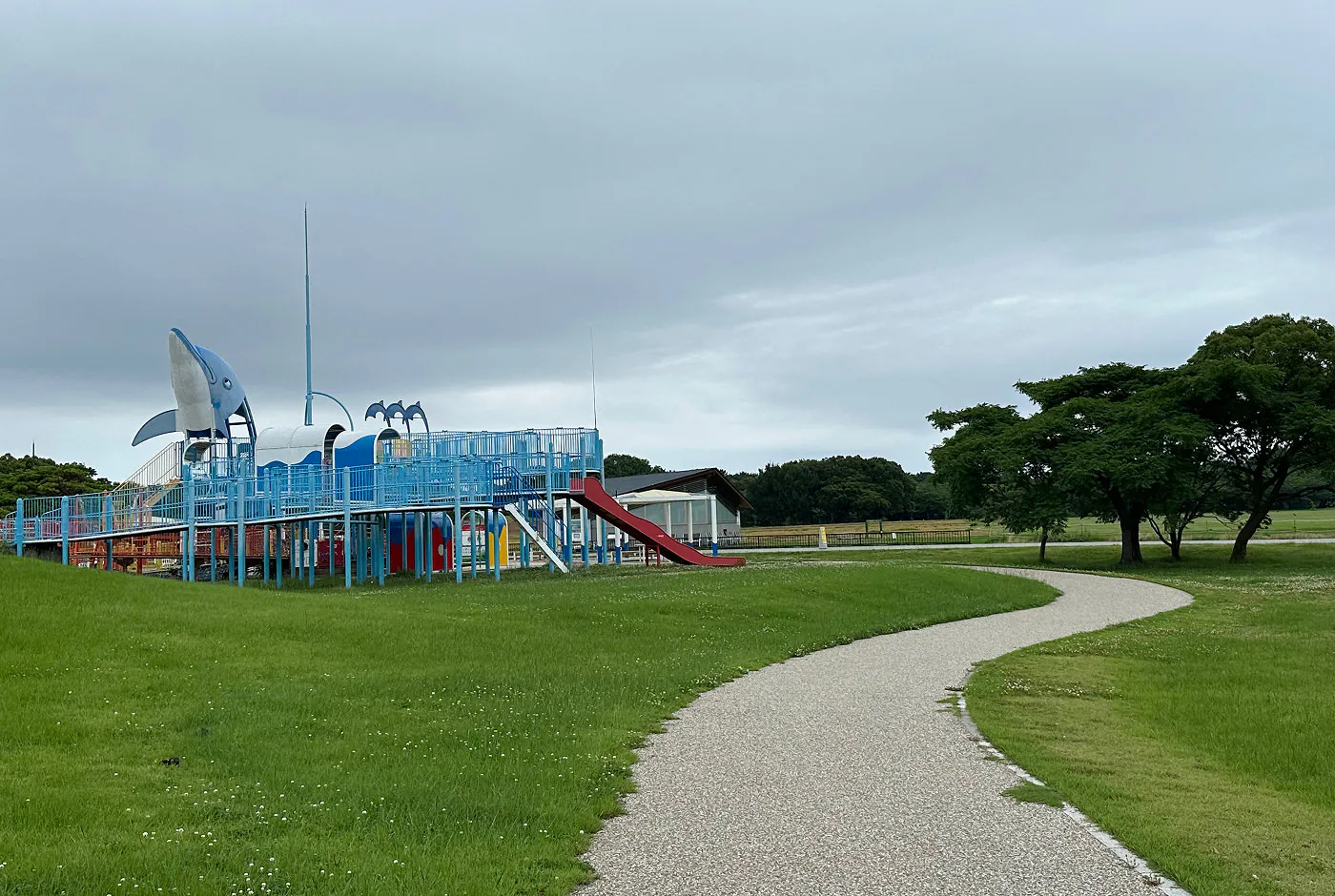 Klätterställning med en staty på en delfin omgiven av en park med välansad gräsmatta och buskiga träd.