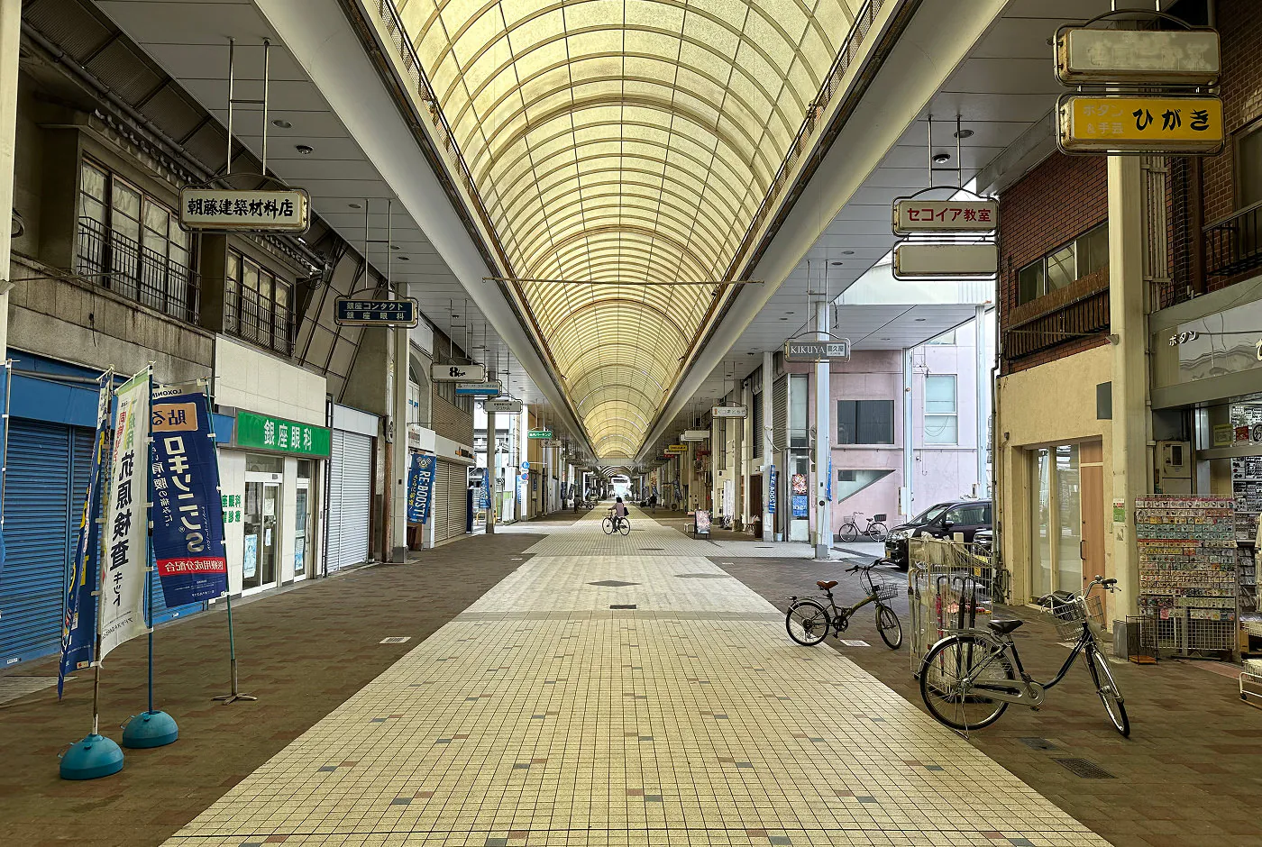 En lång och bred shoppingarkad med högt till tal. Den är helt folktom förutom en ensam cyklist.