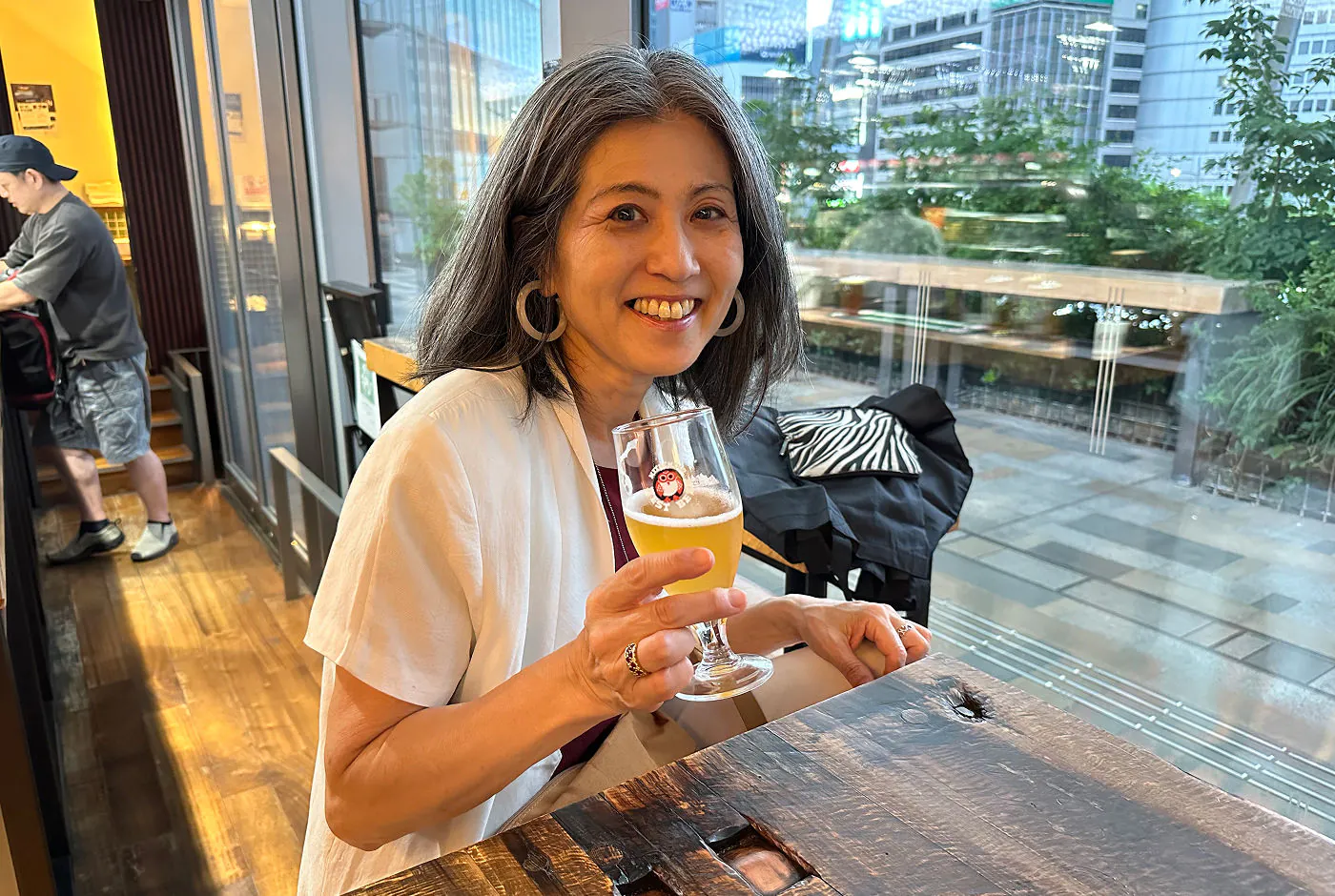 Keiko sitter vid ett bord i en liten bar och dricker en ljus öl. Hon ler in i kameran.