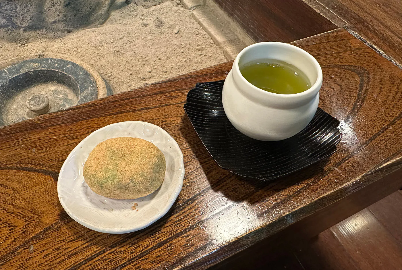 En liten tallrik med en mochi-riskaka och en liten vit kopp med matcha-te.
