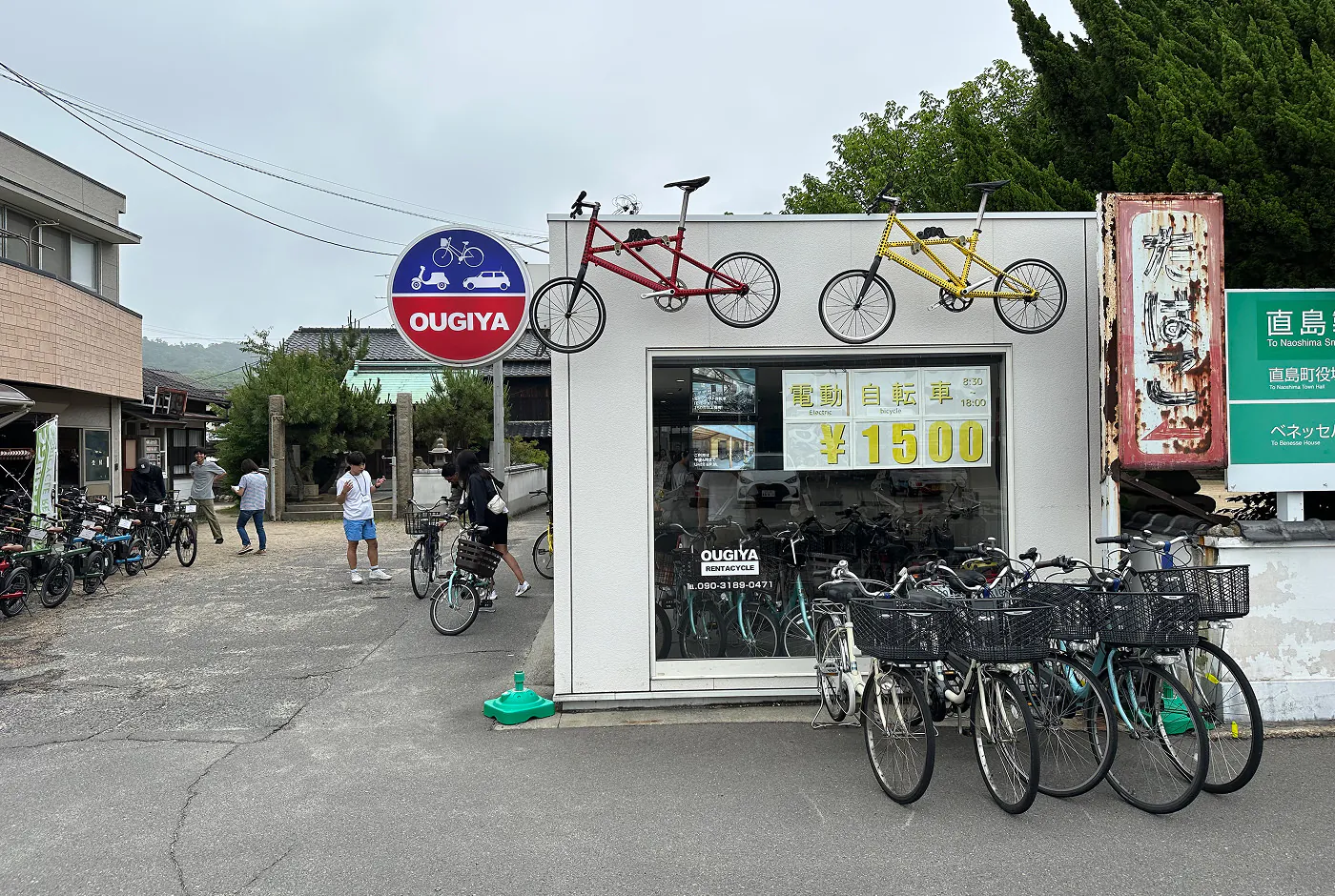Ljus liten butiken cyklar utanför. En rund skylt har texten "Ougiya".
