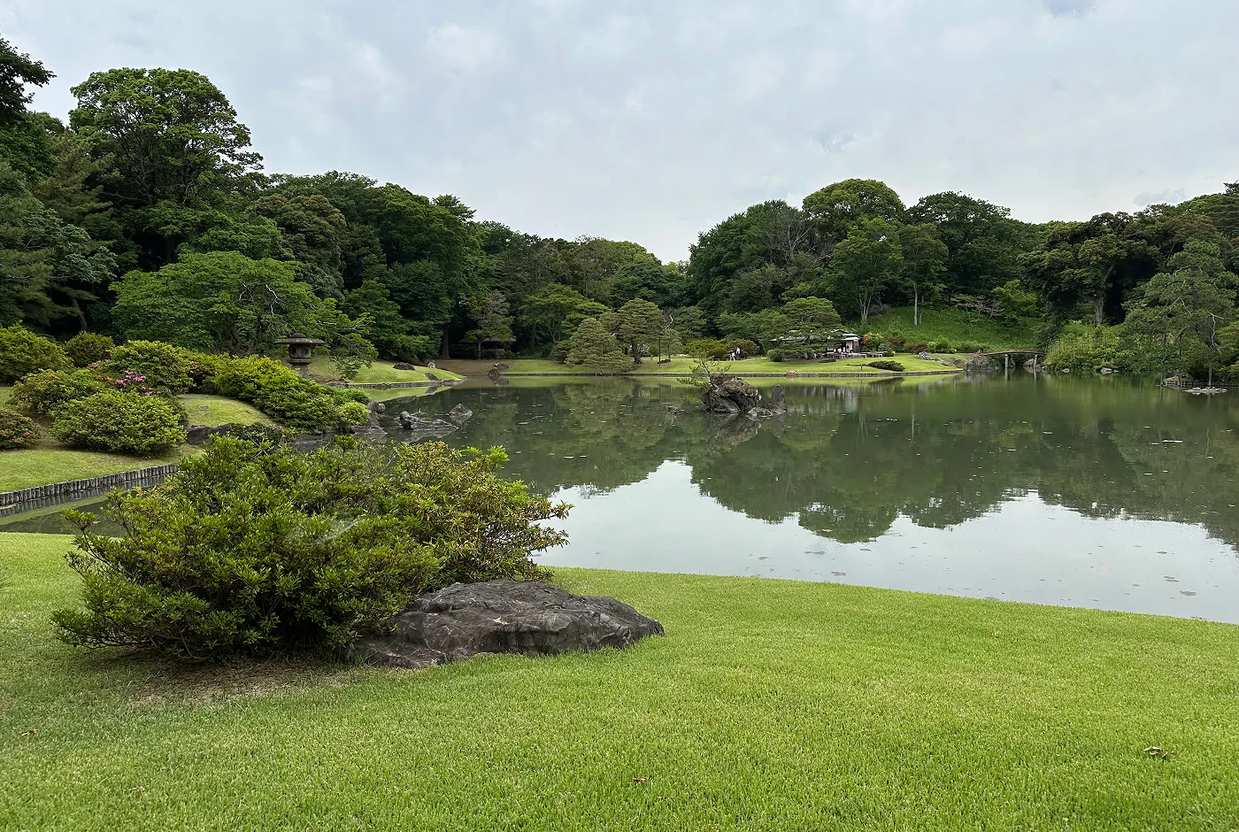 Traditionell japansk trädgård med en stor sjö i mitten omgiven av lummiga träd och buskar.