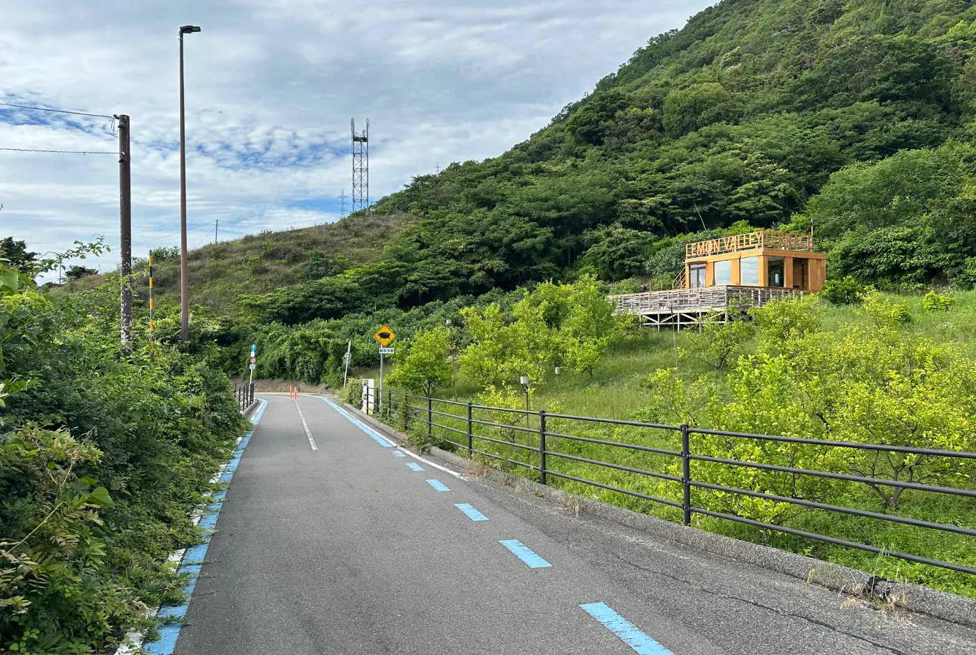 Cykelväg ned för en backe i en lummig dal. En orange byggnad till höger har en skylt som lyder "Lemon Valley".
