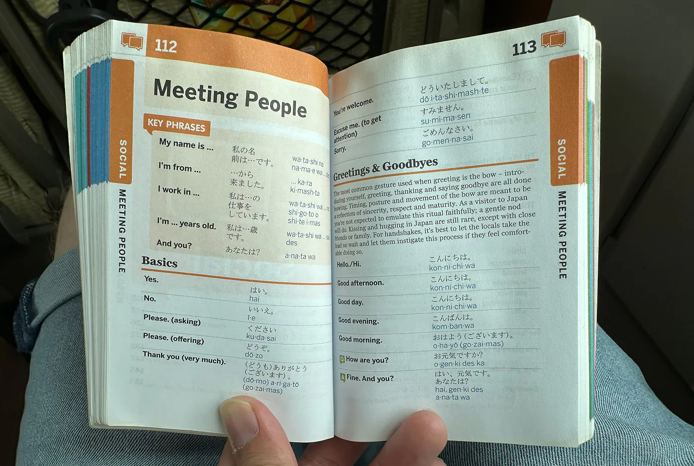 Hand håller upp en bok om japanska för turister. Kapitlet lyder "Meeting People".
