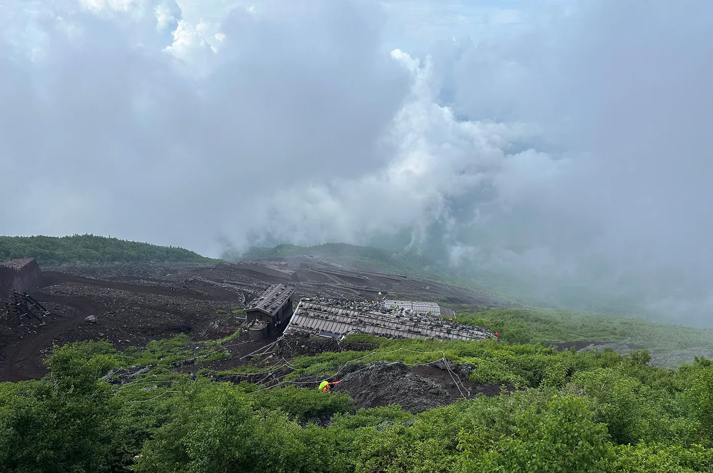 Lummig vandringsled upp för ett massivt berg. Nedanför leden finns flera tre byggnder. I fjärran täcker dimman en dal.