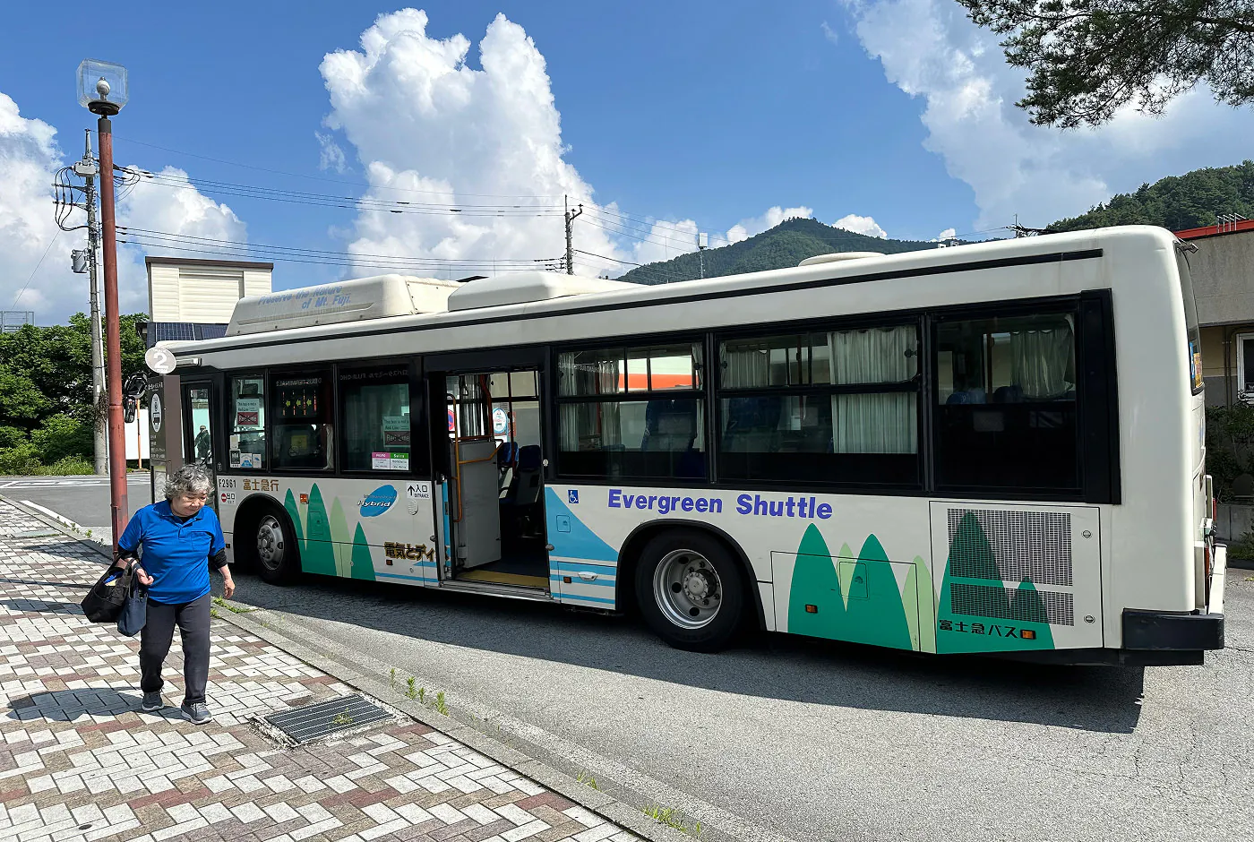 Bit buss har stannat vid en hållplats i en stad. Utanför gör en äldre kvinna med en blå tröja.