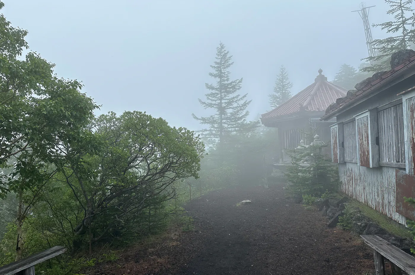 Grusgång förbi två slitna gamla små hus. Det är dimmigt i skogen som omger husen.