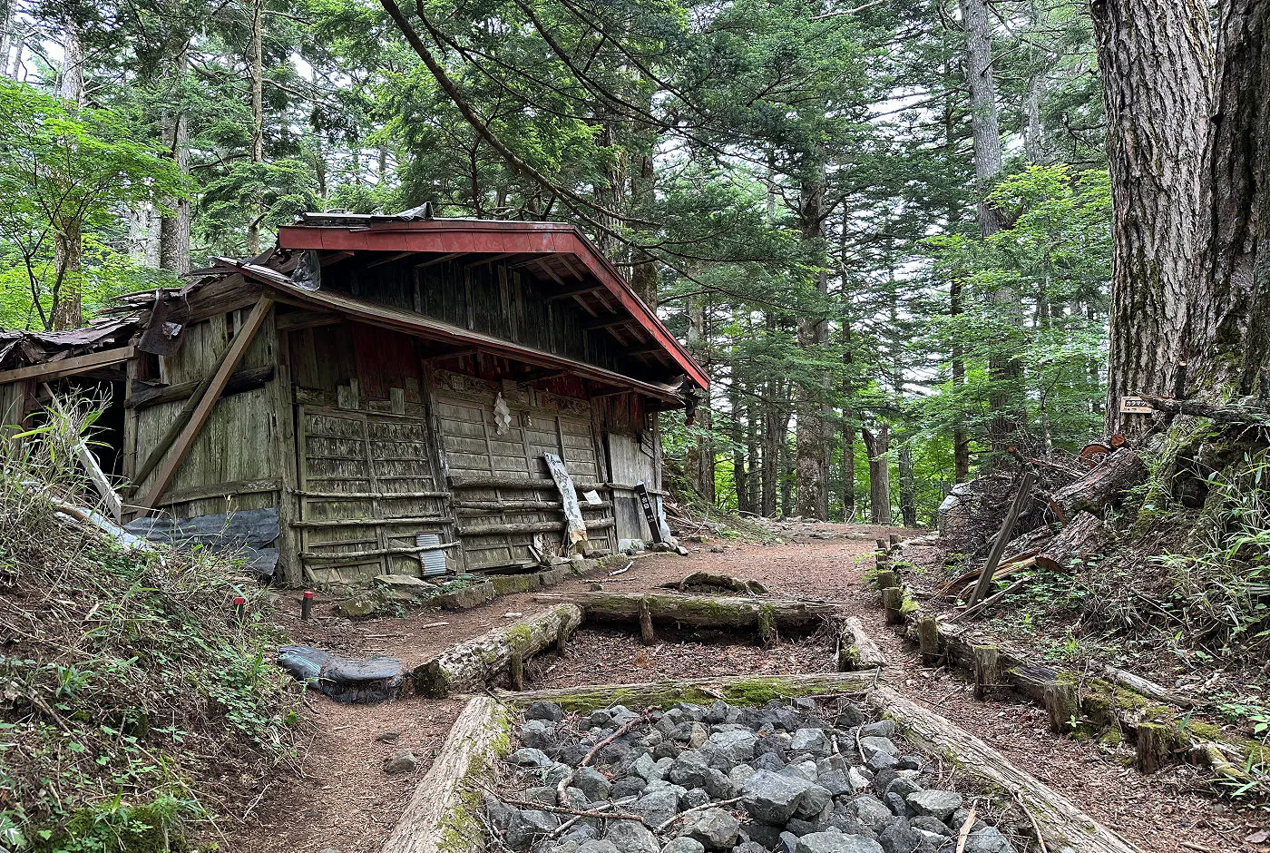 Gammalt och fallfärdigt hus jämte en vandringsled i en skog.