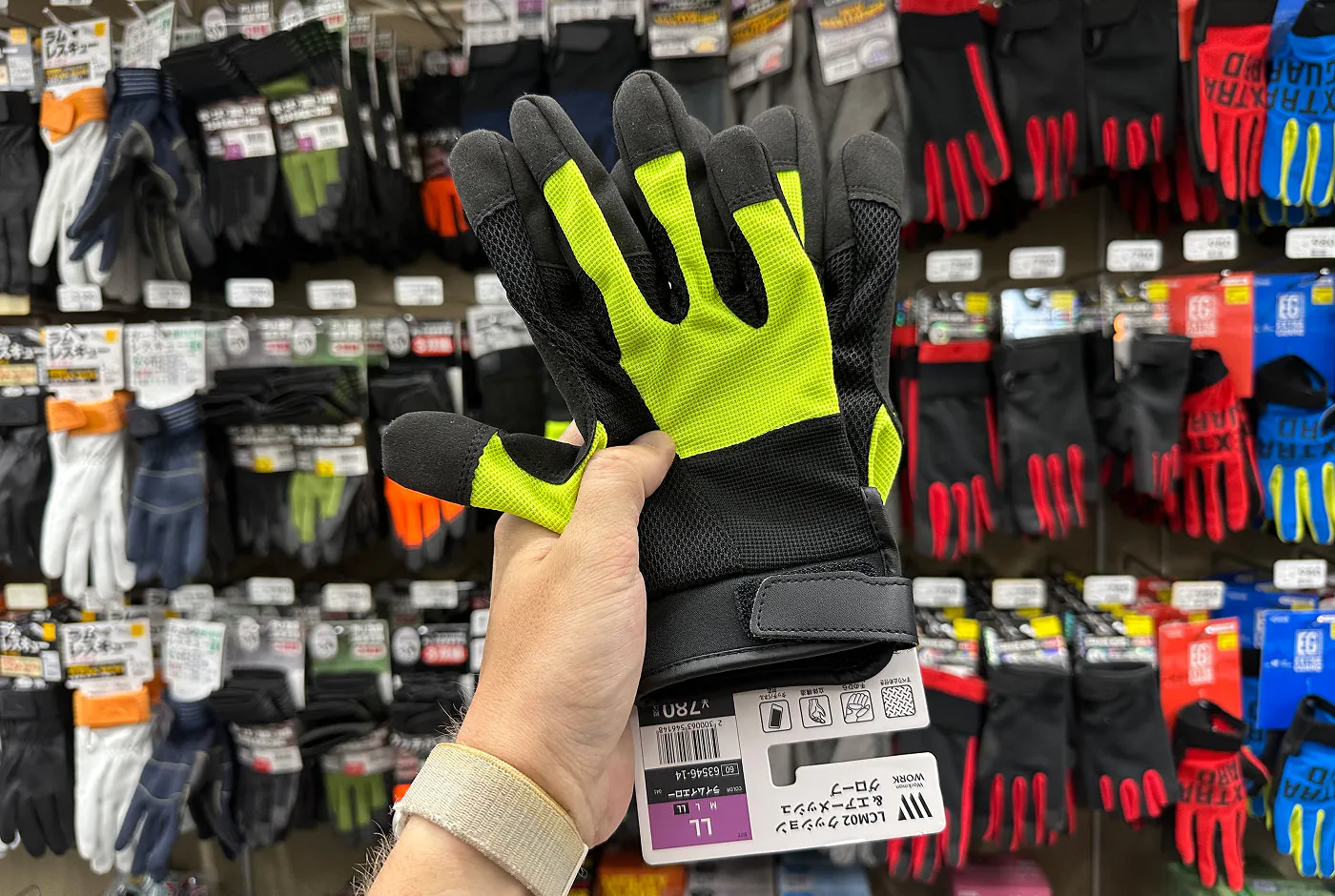 Hand håller i ett par gulsvarta handskar framför en hylla med handskar i olika färger.