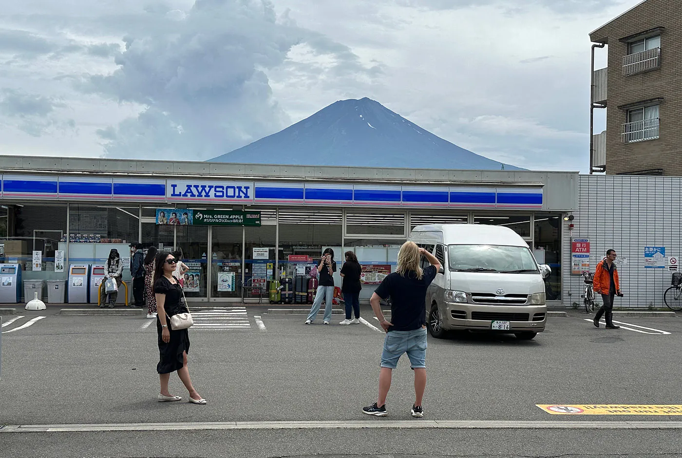 Jag stor på en parkeringsplats utanför en liten matbutik och tittar ut över Mount Fuji. Jag har ryggen åt kameran.
