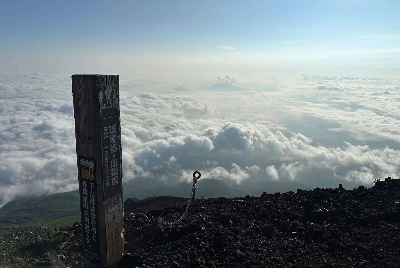 Påle med text på vid en vandringsled. I fjärran syns ett vidöppet landskap täckt av moln.