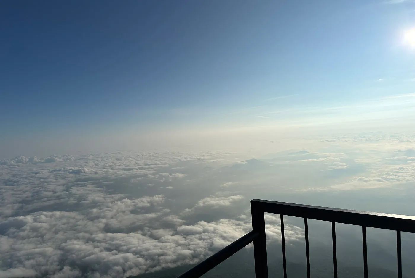 Ett mörkt metallräcke framför ett vidöppet landskap täckt med moln.