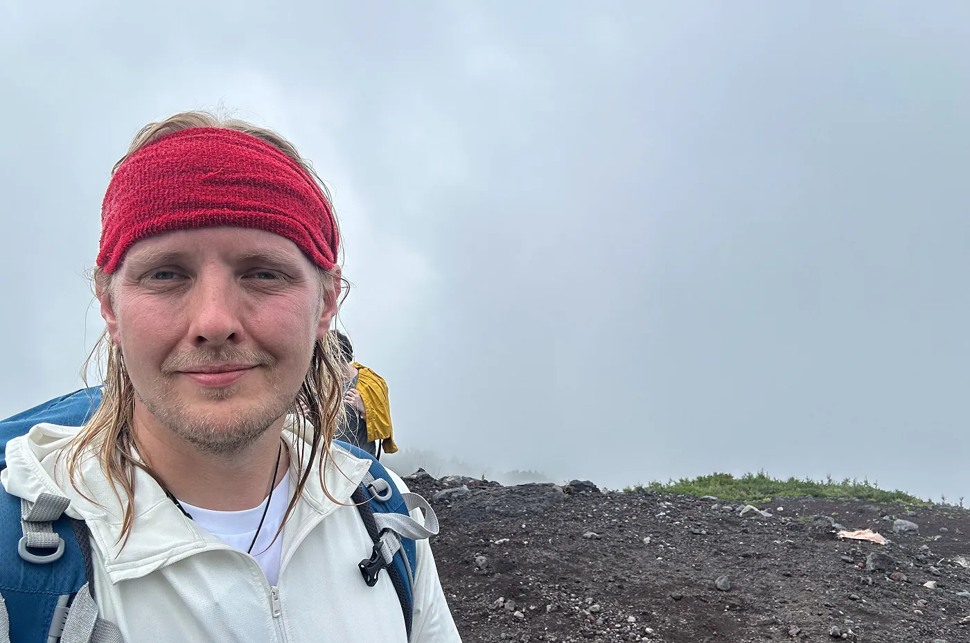 Jag tittar in i kameran och ser lätt besvärad ut. Jag har en vit jacka och ett rött bandana. Bakom mig är det mycket dimma.