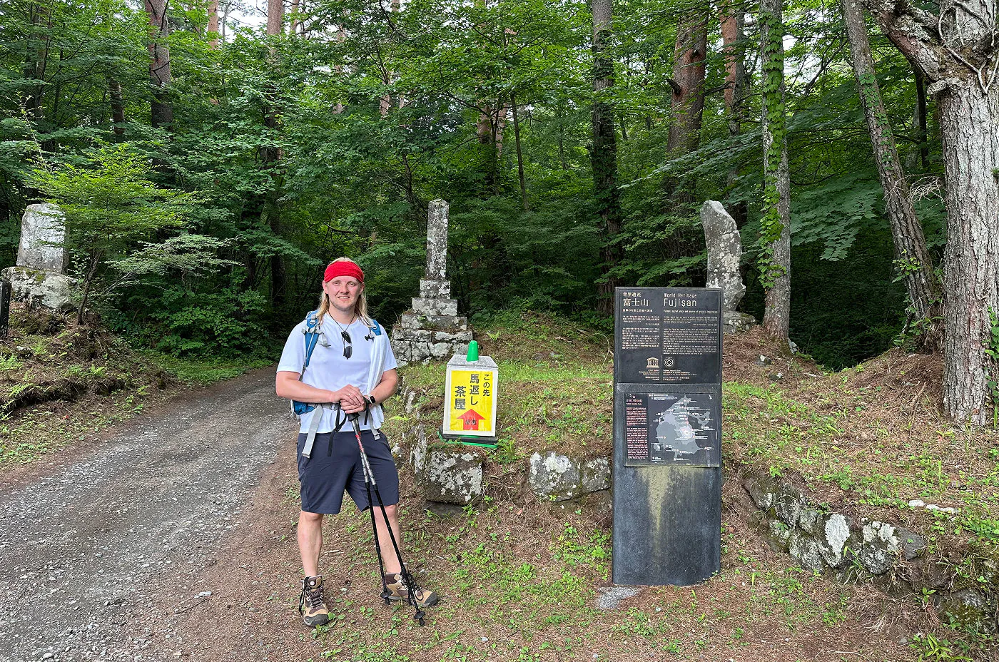 Jag står vid en stig in till en skog och ler mot kameran med vandringskläder på mig.