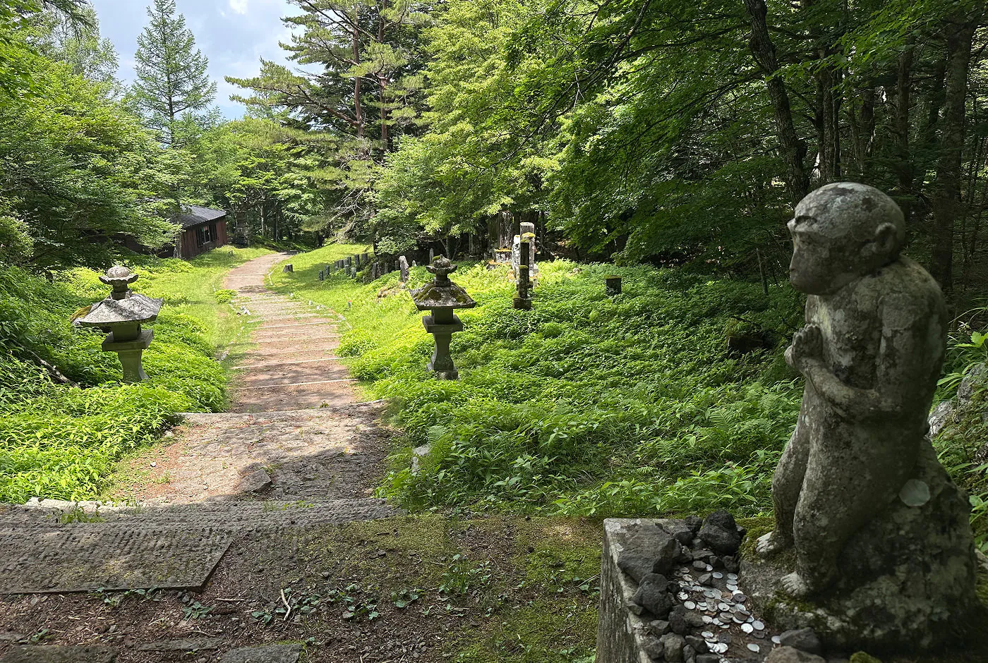 Stengång följt av en stentrappa går genom en skog. På sidorna av gången står stenlyktor, en staty och ett hus.
