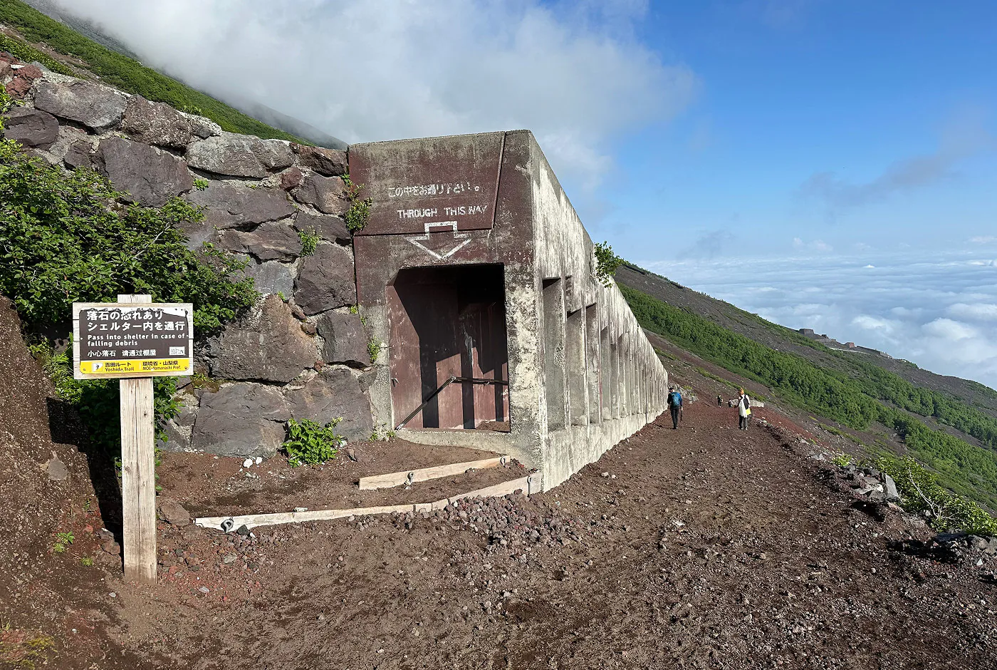Bred grusstig längs med en sluttande berg. En halvöppen betongpassage står till vänster på stigen för att skydda mot ras.