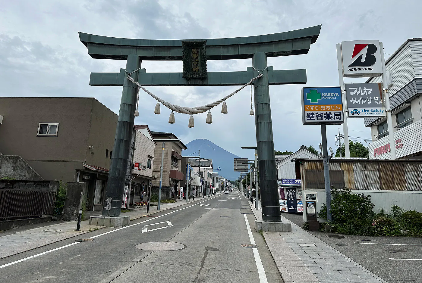 Stor och gråblå torii-port på en lång gata i en stad. I fjärran syns Mount Fuji.