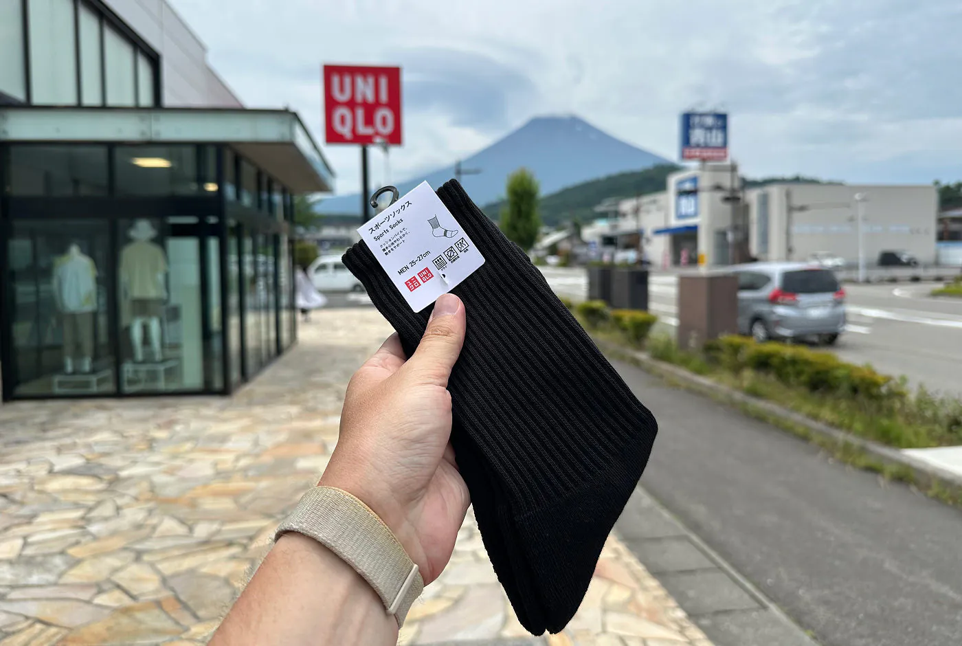 Hand håller i ett par svarta sockor. I fjärran syns Mount Fuji och en röd skylt för butikskedjan Uniqlo.