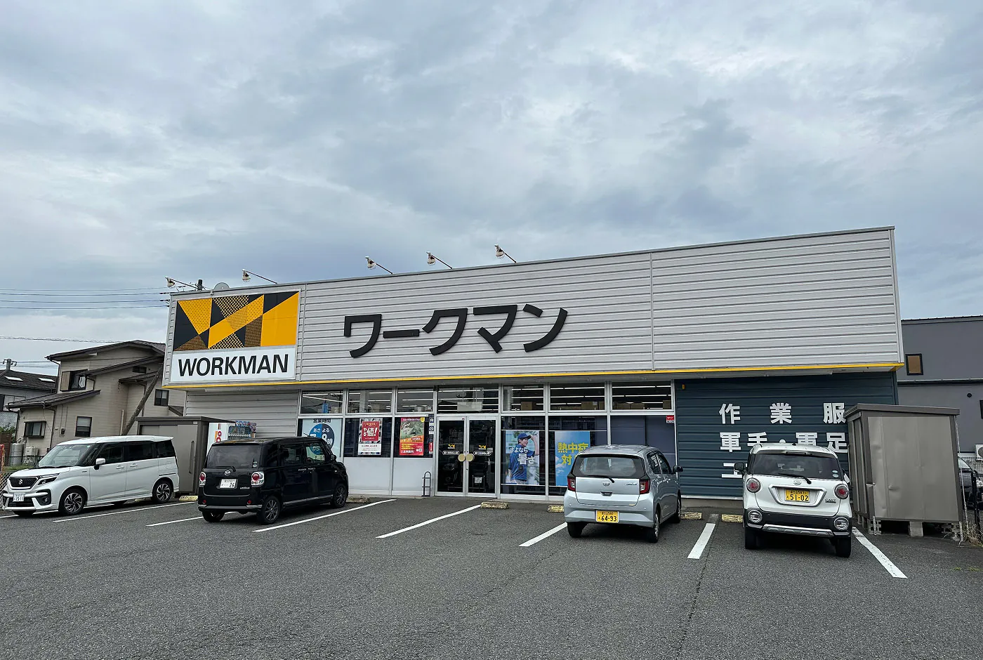 Fyra bilar står parkerade utanför en grå och tråkig fasad med en gul skylt som lyder "Workman".