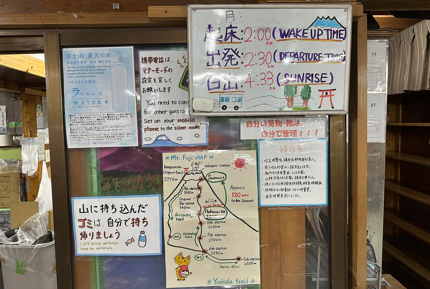 Sju stycken skyltar på en skjutdörr i glas i ett vandrarhem. Skyltarna tar upp tips för att ta sig till Mount Fujis topp samt vett och etikett.