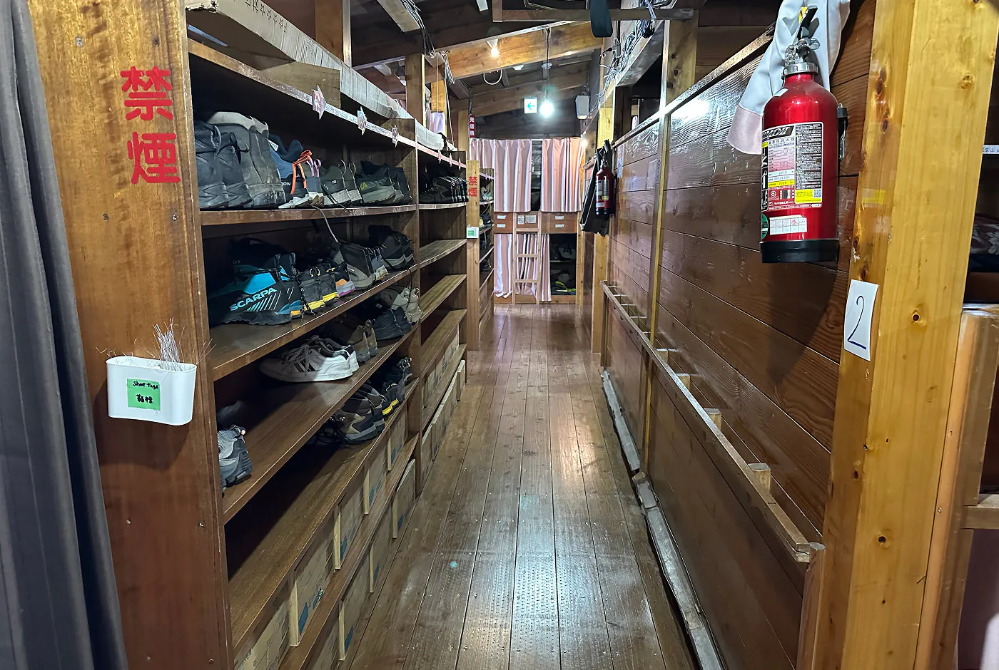 En korridor i ett vandrarhem. Till vänster står skor i en hylla, till höger hänger en brandsläckare och längt bort finns sovplatser.