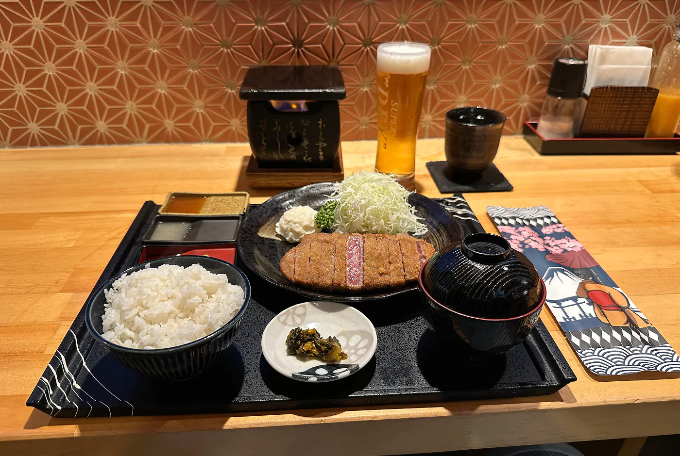 Fyra skålar mat på en svart bricka på en träbänk. Huvudrätten är friterat griskött med ris.