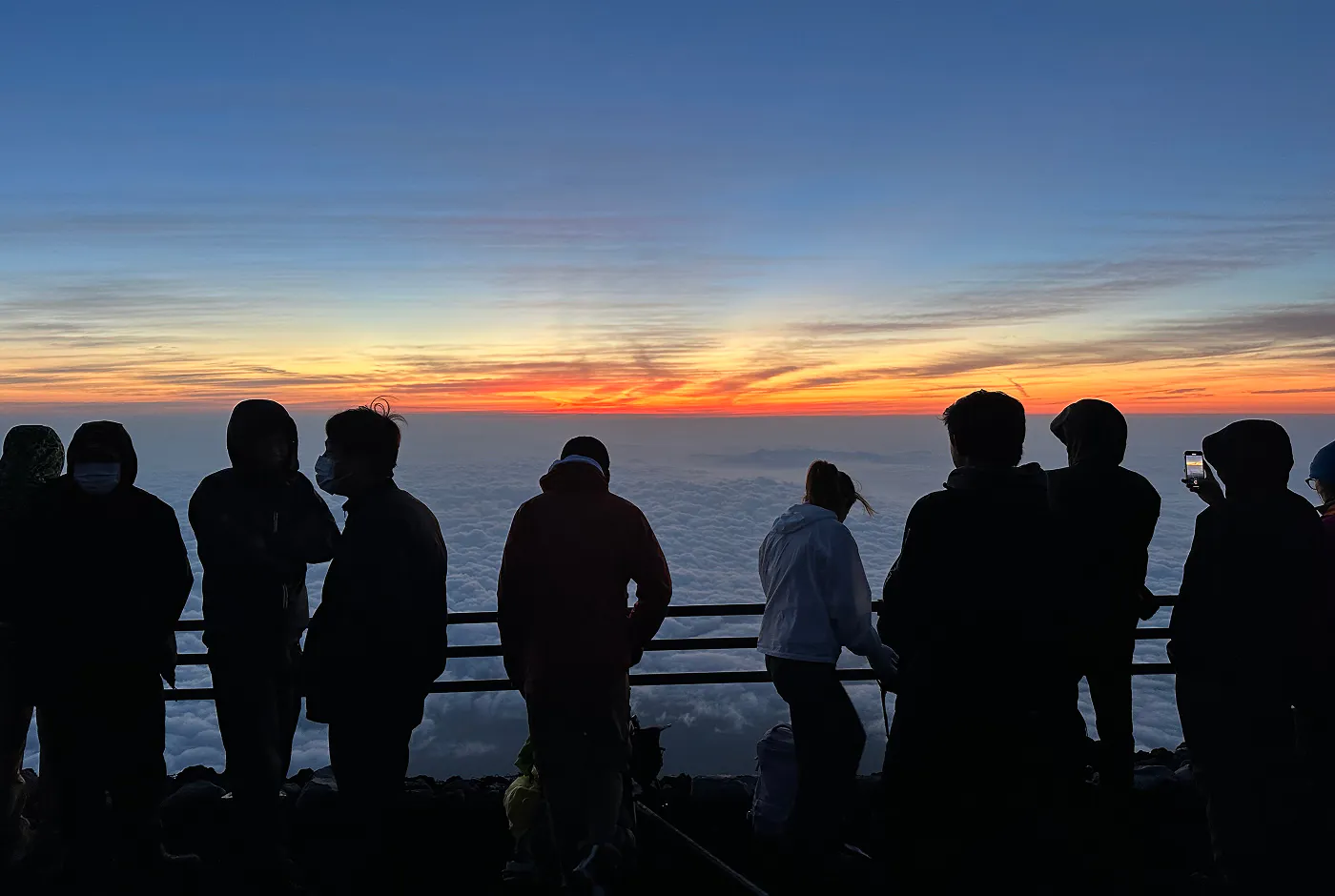 Solietter av tio personer vid ett räcke på toppen av Mount Fuji vid soluppgång.