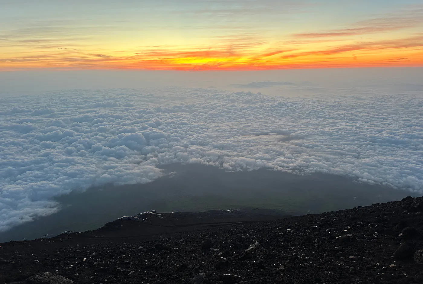 Utsikt över brant berg följt av en grön dal under ett molntäcke. Solen håller på att går upp.
