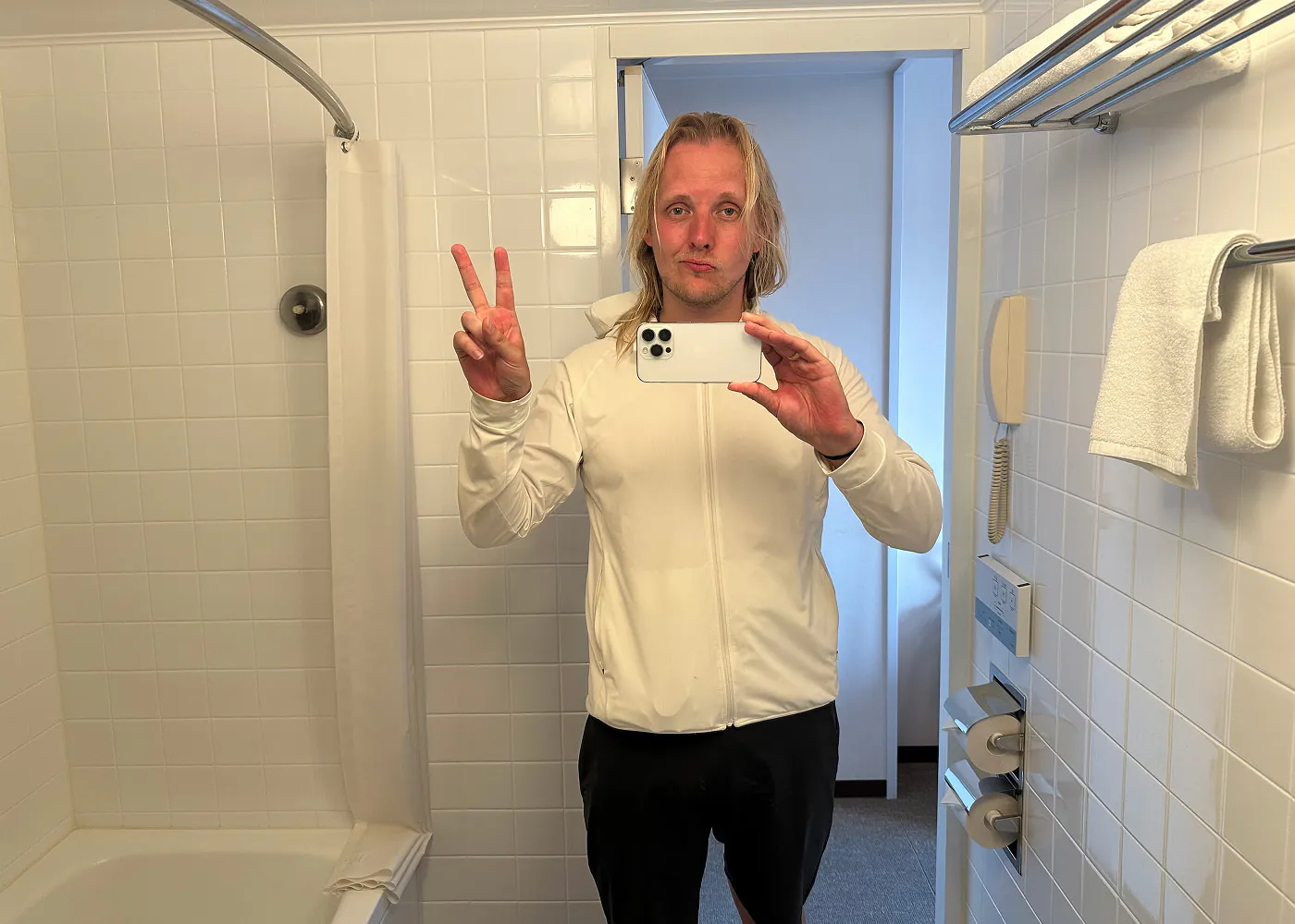 Jag tar en bild på mig själv inuti ett badrum. Jag har svettigt hår och en vit tunn sportjacka på mig.